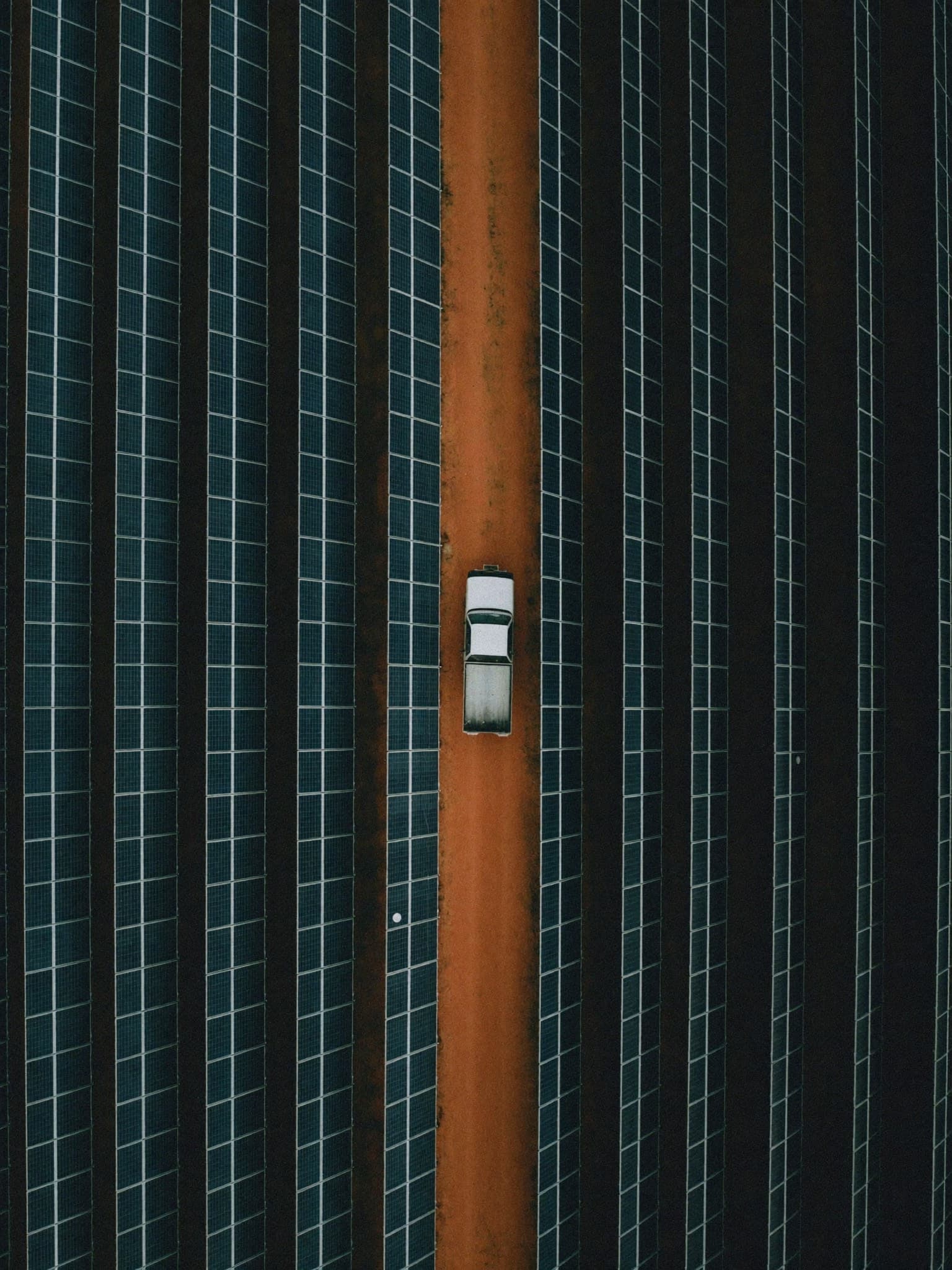 Top-down aerial view of solar panel rows beside a red service road