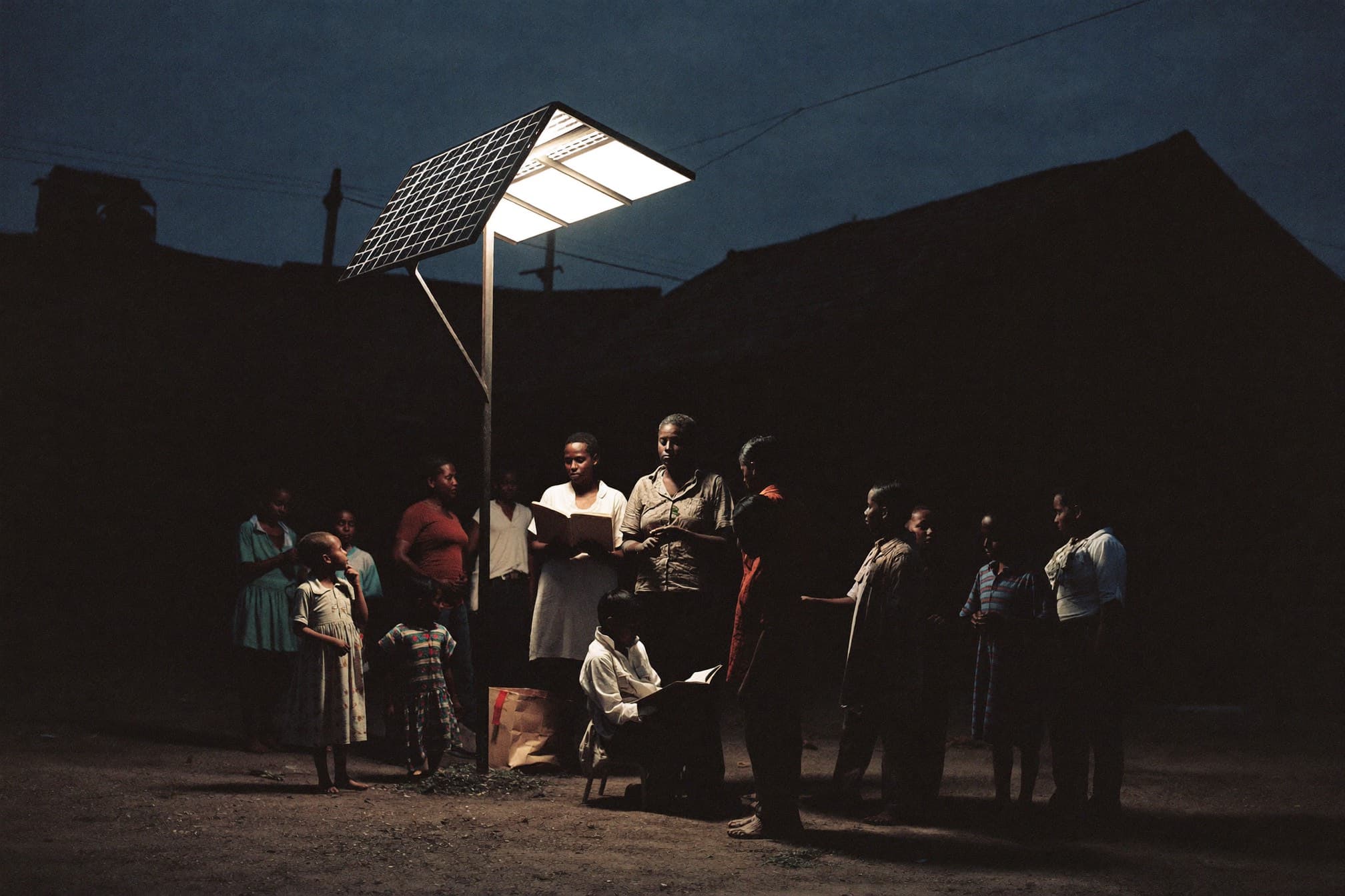 Families gathered under a solar streetlight in a village square at night