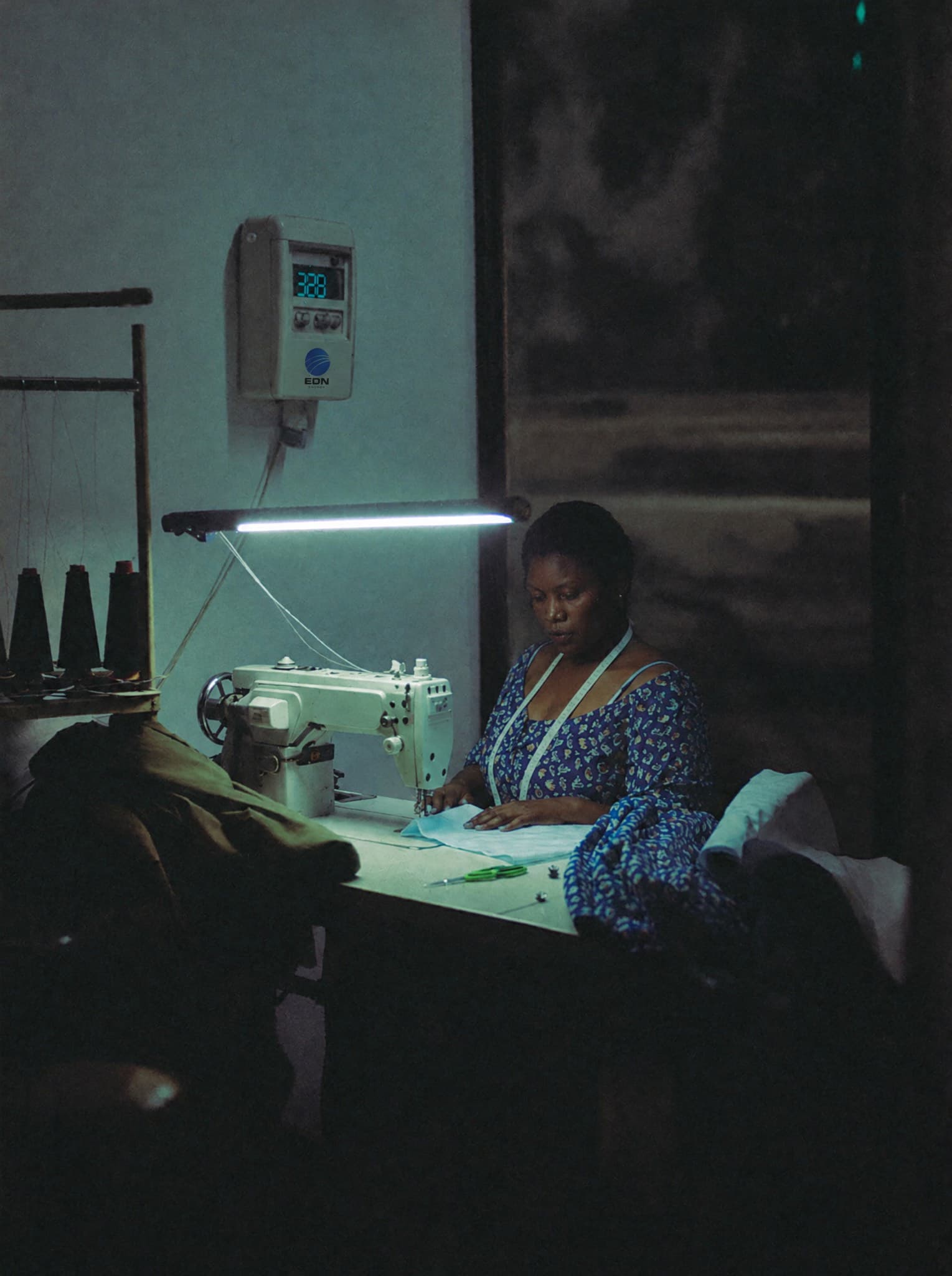 Tailor working at her sewing machine in a shop lit by an LED bulb