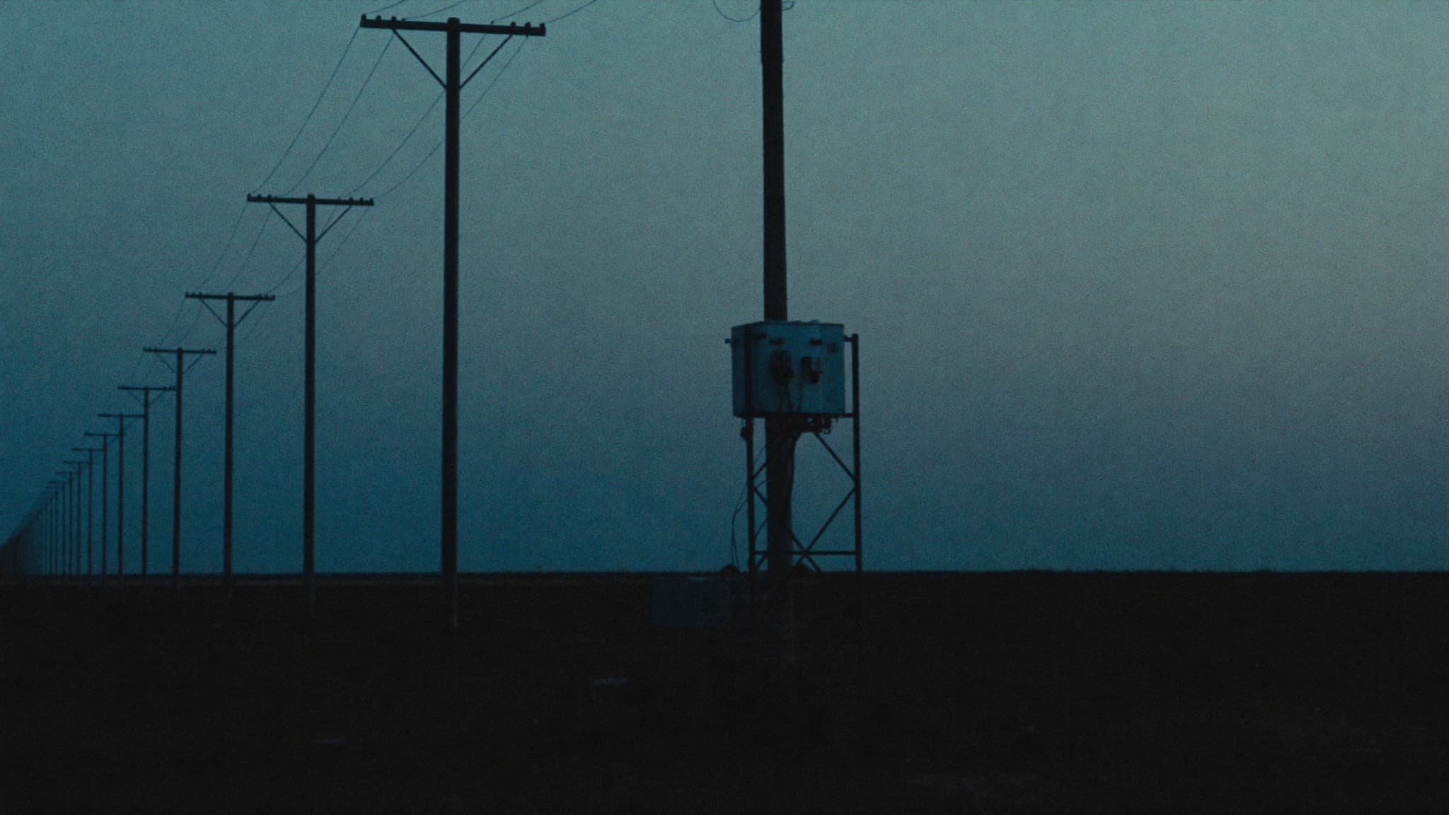 Power poles and a transformer silhouetted over the savanna at dusk