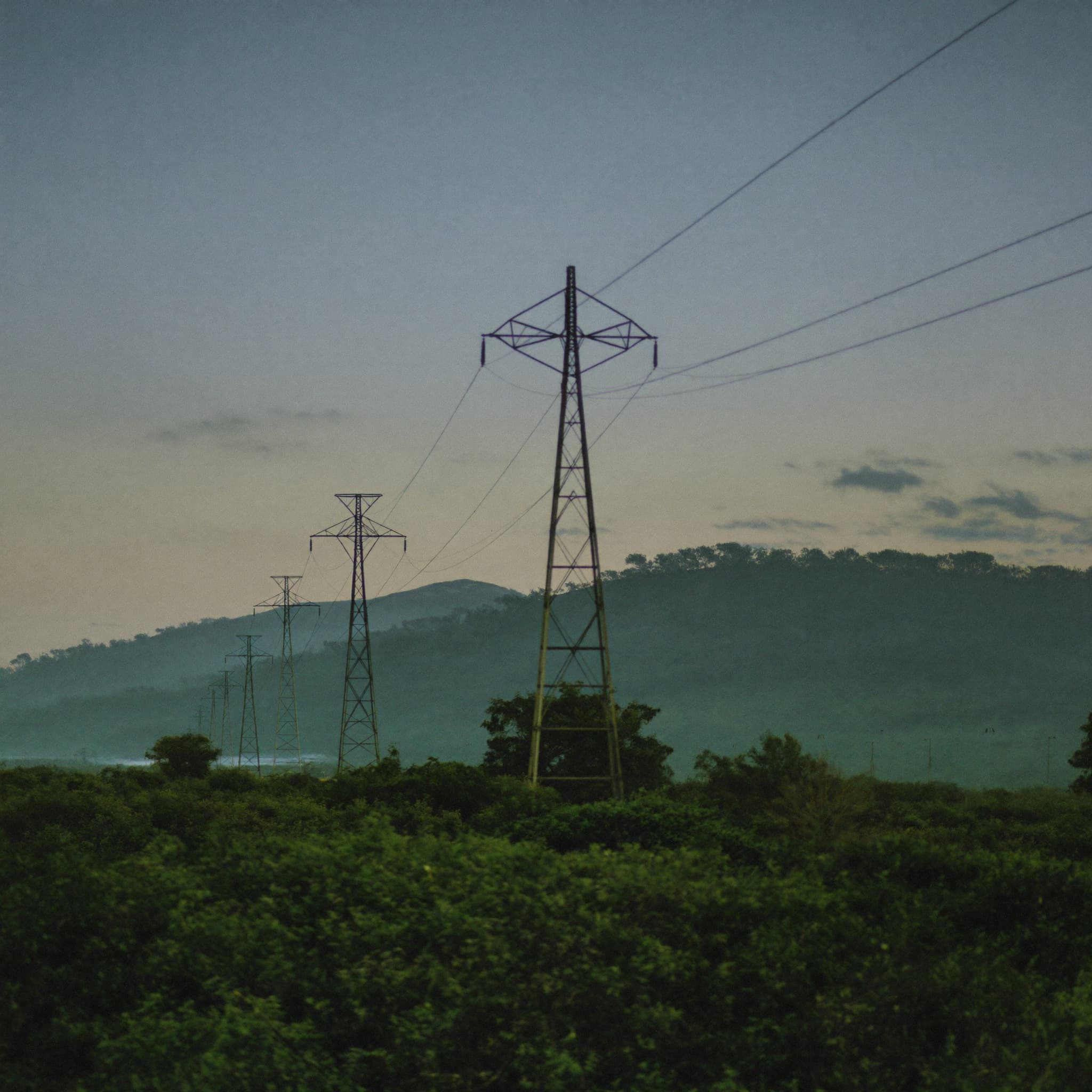 High-voltage power lines crossing green hills at dusk