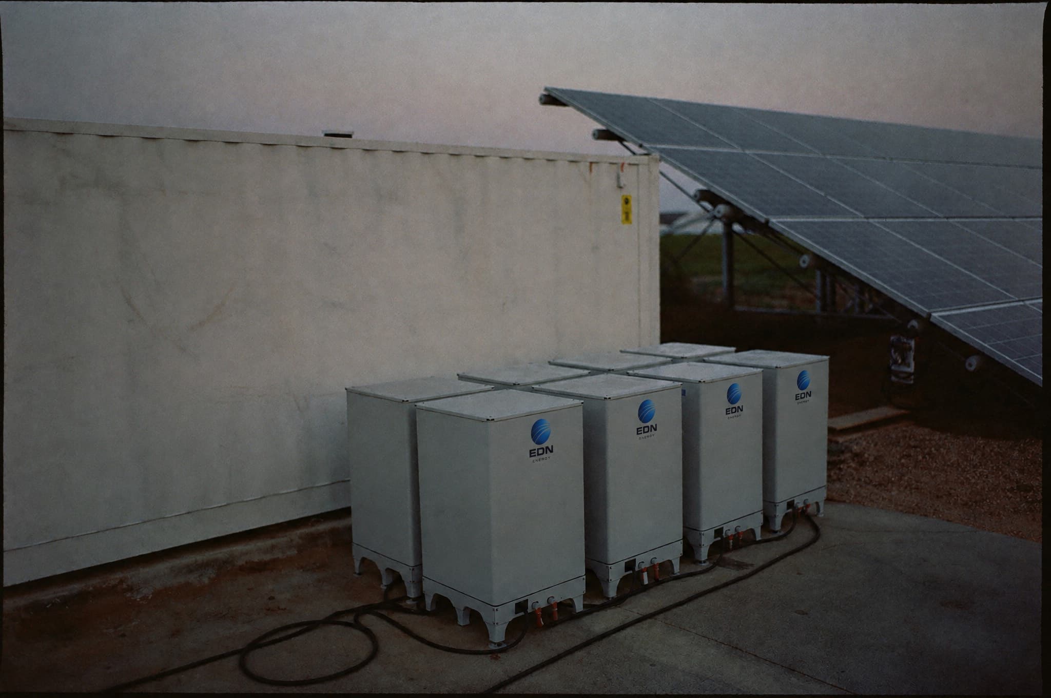 Battery storage units and inverters beside a solar array at dusk
