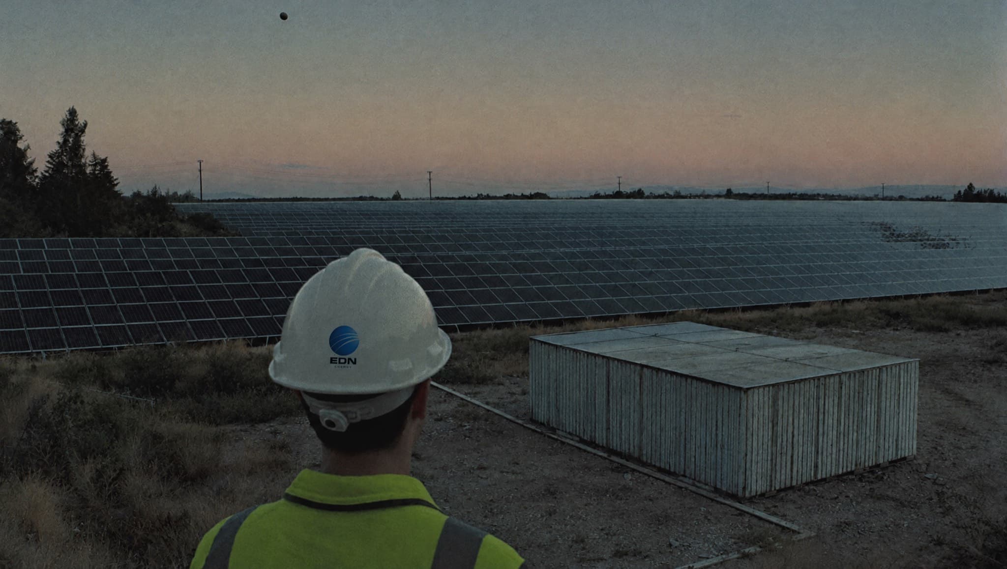 Engineer in a hard hat looking out over a solar farm at dusk